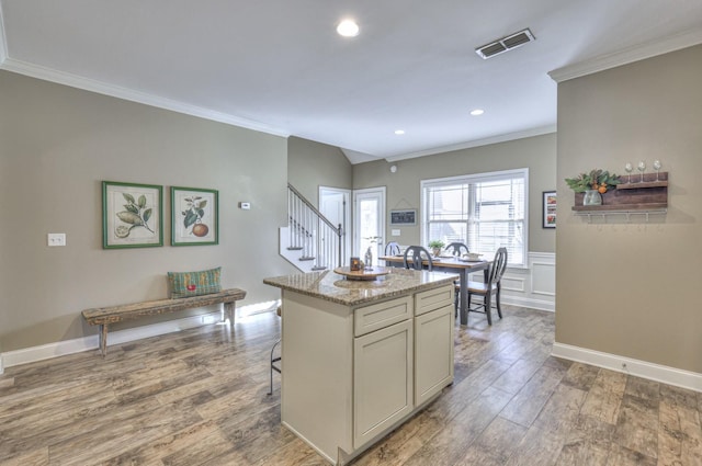 kitchen featuring a breakfast bar, a center island, hardwood / wood-style flooring, light stone countertops, and ornamental molding