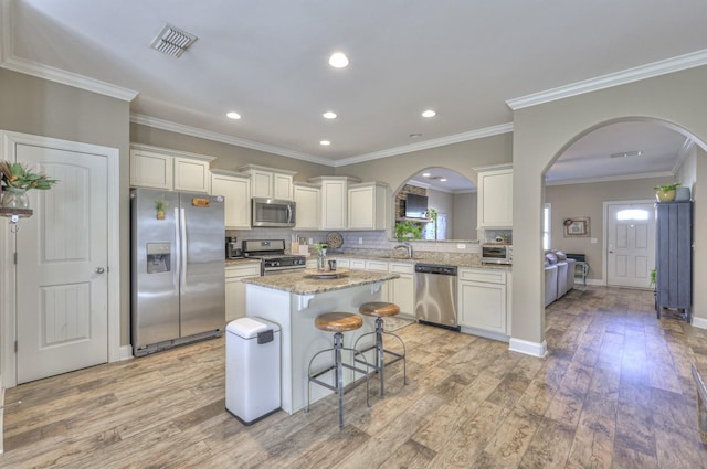 kitchen with ornamental molding, stainless steel appliances, sink, a kitchen island, and a breakfast bar area