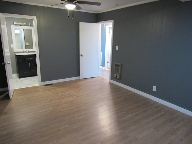 unfurnished bedroom with connected bathroom, ceiling fan, sink, heating unit, and hardwood / wood-style flooring