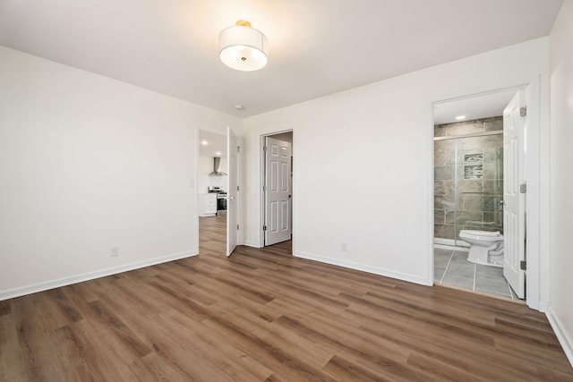 unfurnished bedroom featuring ensuite bathroom and dark hardwood / wood-style flooring