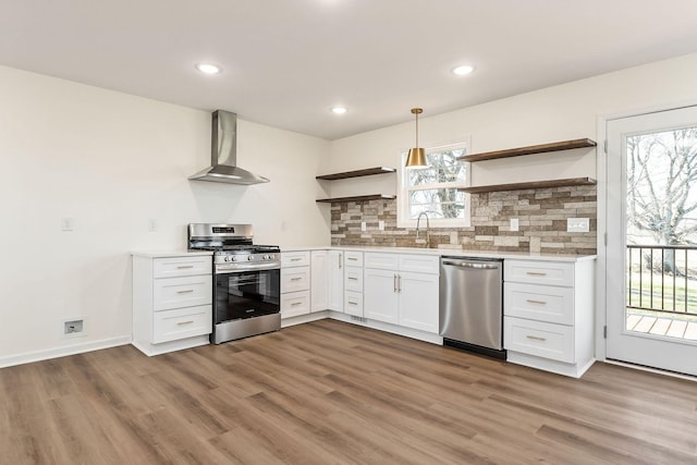 kitchen with tasteful backsplash, wall chimney exhaust hood, stainless steel appliances, white cabinets, and hanging light fixtures