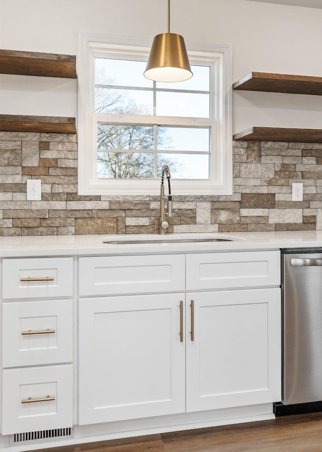 kitchen with backsplash, sink, hanging light fixtures, stainless steel dishwasher, and white cabinetry