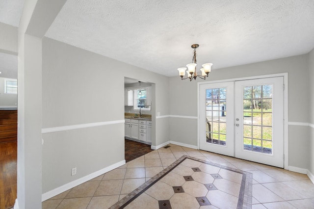 unfurnished dining area featuring french doors, sink, a chandelier, a textured ceiling, and light tile patterned floors