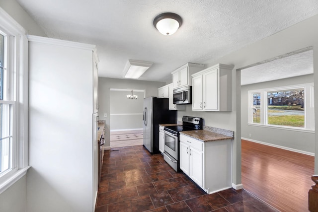 kitchen with dark stone counters, an inviting chandelier, a textured ceiling, appliances with stainless steel finishes, and white cabinetry