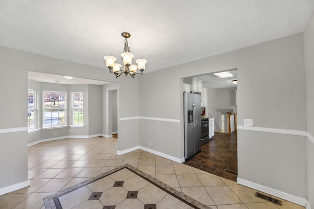 unfurnished dining area with dark tile patterned floors, a textured ceiling, and an inviting chandelier