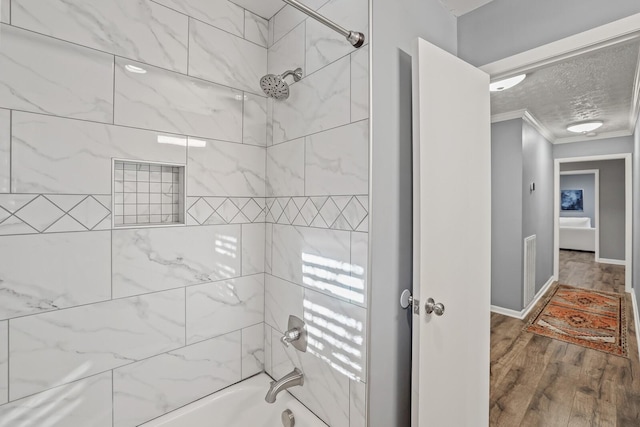 bathroom with hardwood / wood-style floors, a textured ceiling, tiled shower / bath, and crown molding