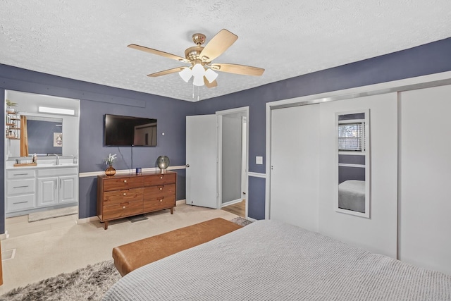 bedroom featuring ceiling fan, a textured ceiling, connected bathroom, and light carpet