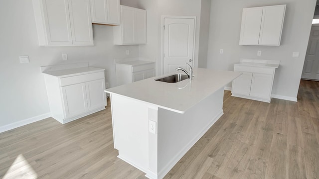 kitchen with white cabinets, sink, light hardwood / wood-style floors, and an island with sink