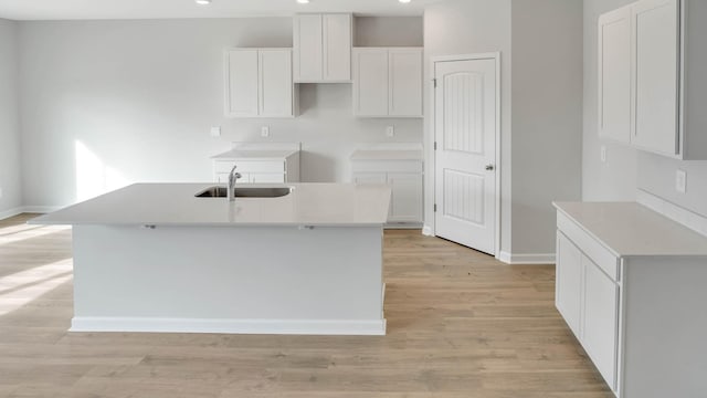 kitchen with light hardwood / wood-style flooring, white cabinetry, a kitchen island with sink, and sink