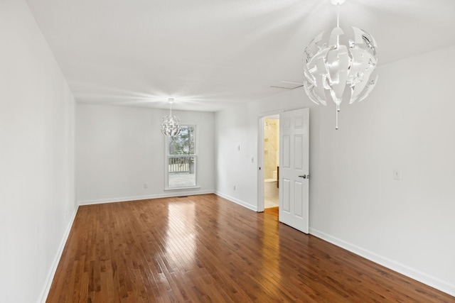 spare room featuring an inviting chandelier and dark wood-type flooring