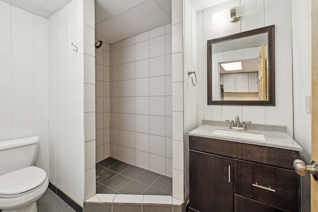 bathroom with tiled shower, vanity, toilet, and tile walls