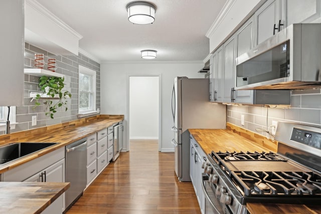 kitchen with crown molding, appliances with stainless steel finishes, dark hardwood / wood-style floors, and butcher block countertops