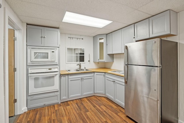 kitchen featuring dark hardwood / wood-style flooring, a drop ceiling, white appliances, wooden counters, and sink