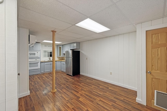 interior space with a drop ceiling, sink, white appliances, and dark hardwood / wood-style floors