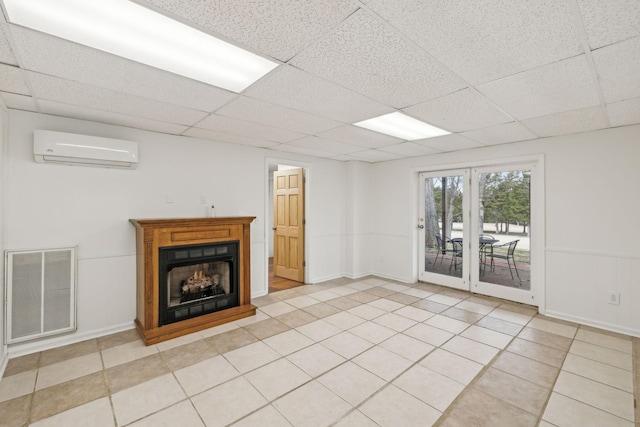 unfurnished living room with light tile patterned flooring, a wall unit AC, and a drop ceiling