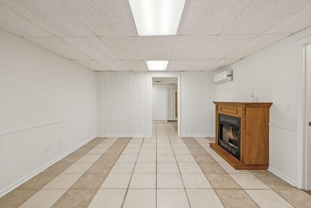 basement featuring a paneled ceiling, a wall unit AC, and light tile patterned flooring