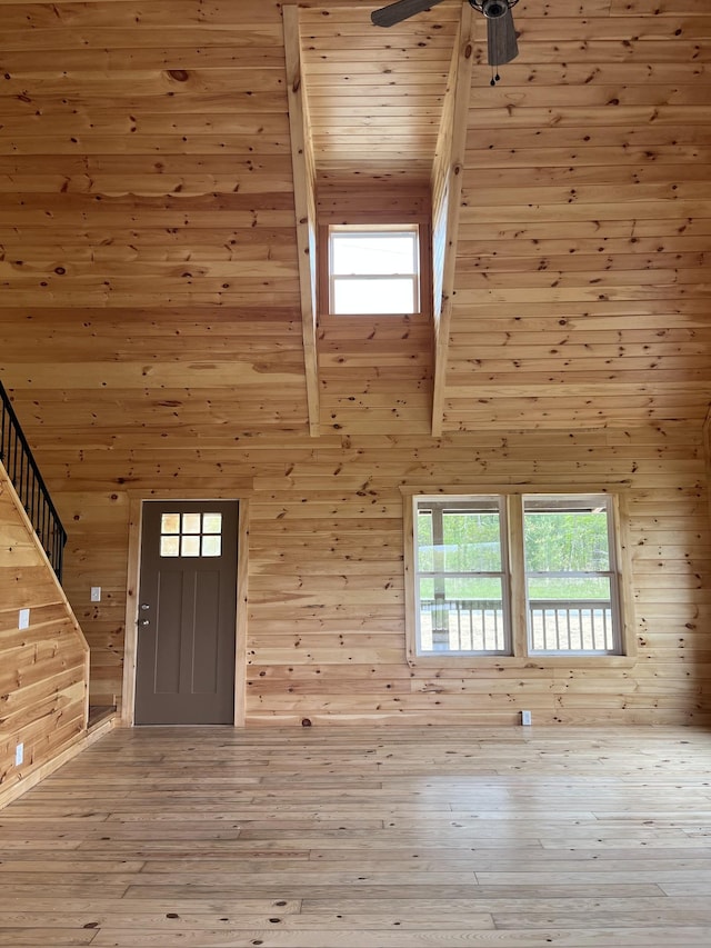 entrance foyer featuring a high ceiling, plenty of natural light, light wood-type flooring, and wood walls