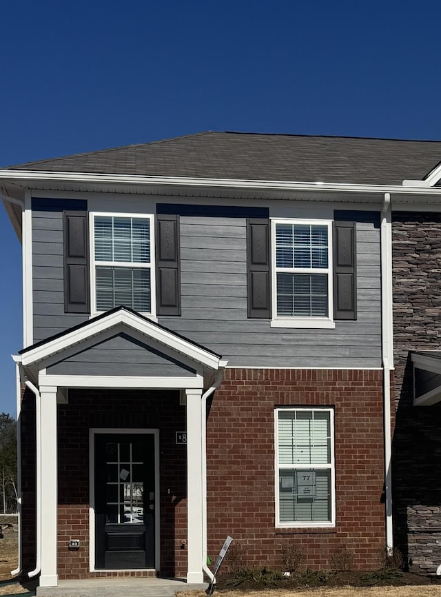 view of front of house featuring brick siding and roof with shingles