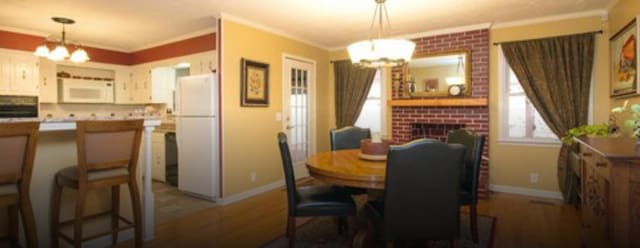 dining room featuring a fireplace, hardwood / wood-style flooring, crown molding, and a notable chandelier