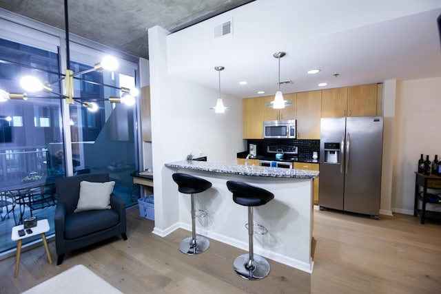 kitchen featuring light hardwood / wood-style flooring, light stone countertops, a kitchen bar, kitchen peninsula, and stainless steel appliances