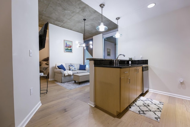 kitchen with kitchen peninsula, light wood-type flooring, stainless steel dishwasher, sink, and pendant lighting