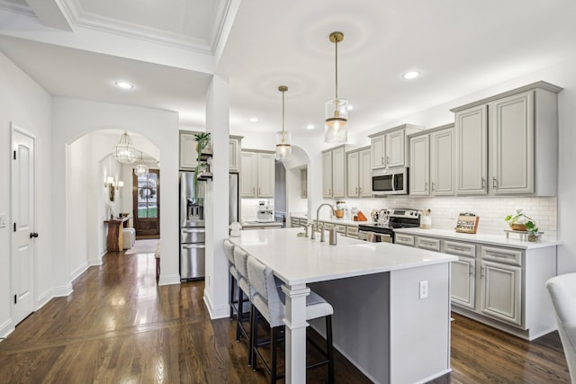 kitchen with gray cabinetry, stainless steel appliances, decorative light fixtures, decorative backsplash, and a breakfast bar