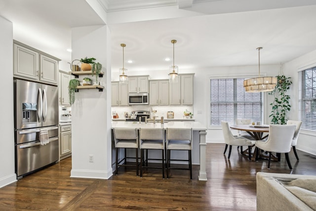 kitchen with a kitchen bar, appliances with stainless steel finishes, dark hardwood / wood-style floors, and pendant lighting