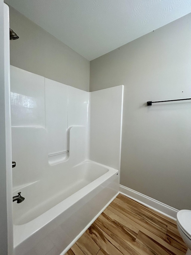 bathroom with washtub / shower combination, hardwood / wood-style flooring, and toilet