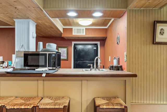 kitchen featuring sink, crown molding, wood walls, black refrigerator, and wood ceiling