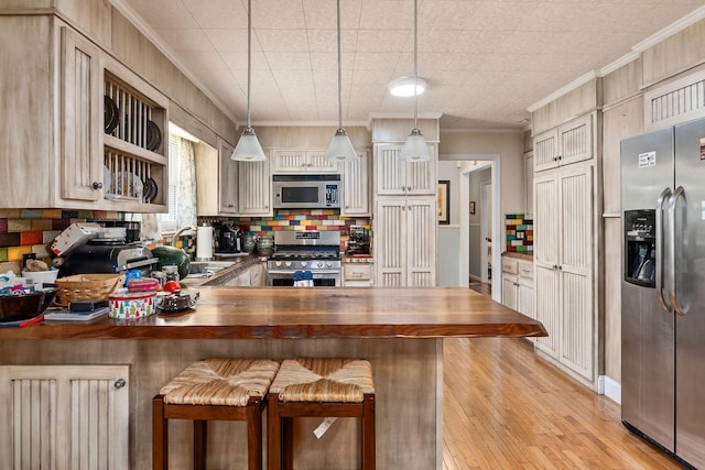 kitchen featuring sink, butcher block countertops, pendant lighting, a kitchen bar, and appliances with stainless steel finishes