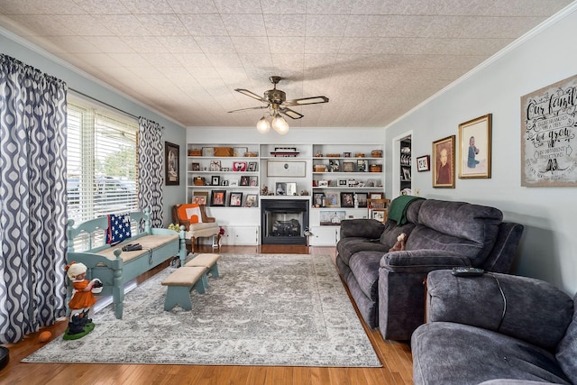 living room featuring ceiling fan, light hardwood / wood-style floors, built in features, and crown molding