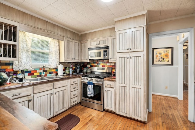 kitchen featuring stainless steel gas range oven, sink, light hardwood / wood-style flooring, decorative backsplash, and ornamental molding