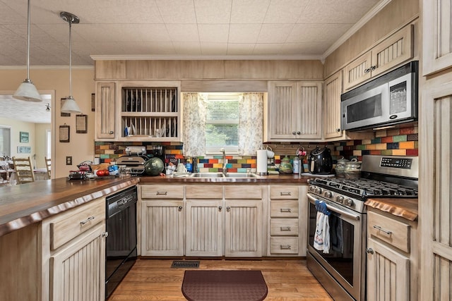 kitchen with ornamental molding, stainless steel appliances, sink, pendant lighting, and butcher block counters