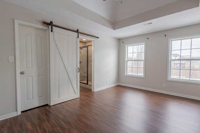 unfurnished bedroom with ceiling fan, ensuite bathroom, a barn door, and dark hardwood / wood-style flooring