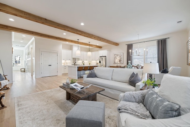 living room featuring beam ceiling, light wood-type flooring, and sink