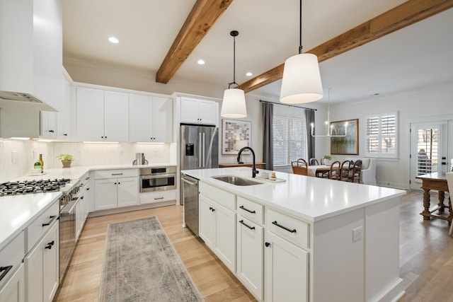 kitchen featuring a kitchen island with sink, white cabinets, sink, hanging light fixtures, and stainless steel appliances