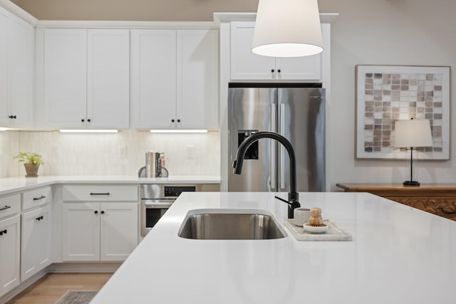 kitchen featuring white cabinetry, sink, light hardwood / wood-style flooring, decorative backsplash, and appliances with stainless steel finishes