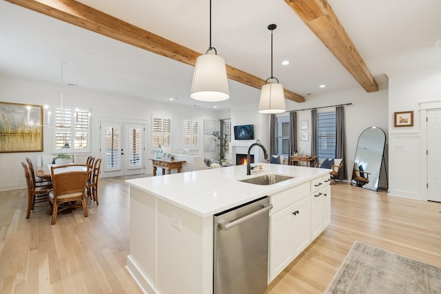 kitchen featuring dishwasher, a center island with sink, sink, hanging light fixtures, and white cabinetry