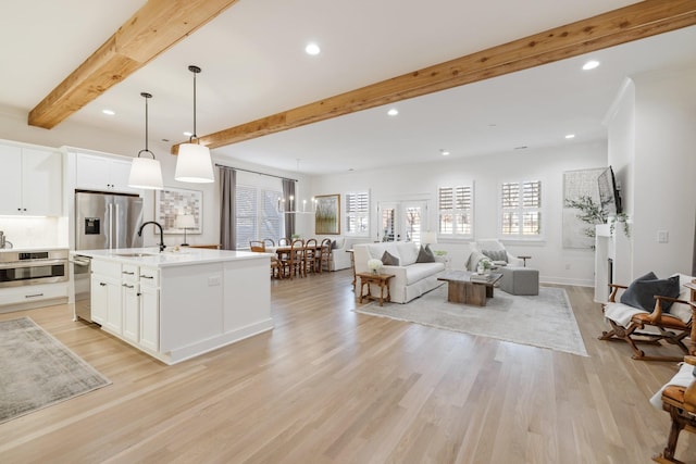 kitchen featuring decorative light fixtures, a center island with sink, white cabinetry, and light hardwood / wood-style flooring