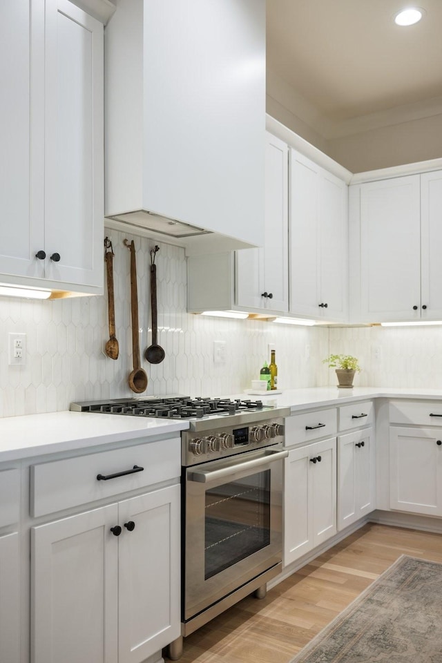 kitchen featuring decorative backsplash, light hardwood / wood-style floors, custom range hood, stainless steel stove, and white cabinetry