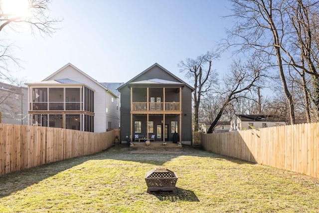 rear view of property with a lawn, a sunroom, and a fire pit