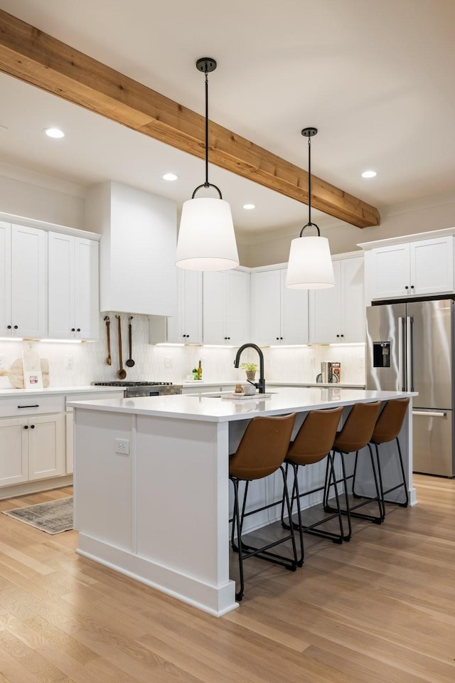 kitchen with beamed ceiling, stainless steel fridge, a center island with sink, and pendant lighting