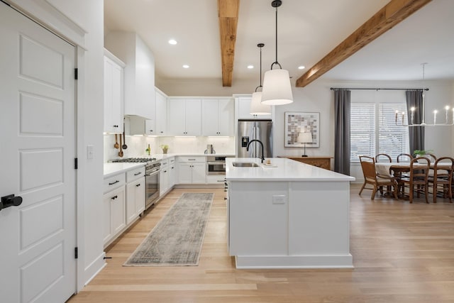 kitchen featuring white cabinets, a center island with sink, hanging light fixtures, appliances with stainless steel finishes, and beam ceiling