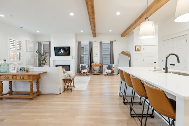 kitchen with sink, hanging light fixtures, beamed ceiling, a fireplace, and light wood-type flooring