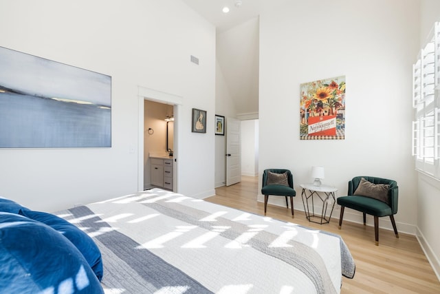 bedroom with ensuite bathroom, light hardwood / wood-style floors, and high vaulted ceiling