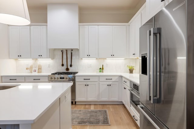 kitchen featuring premium appliances, light wood-type flooring, white cabinetry, and backsplash