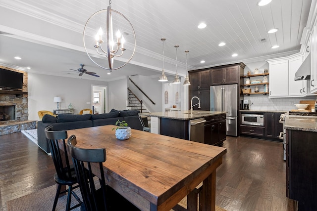 dining room featuring a stone fireplace, crown molding, dark wood-type flooring, and ceiling fan with notable chandelier