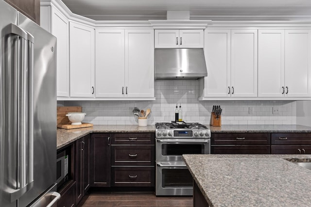 kitchen with ventilation hood, tasteful backsplash, premium appliances, light stone counters, and white cabinetry