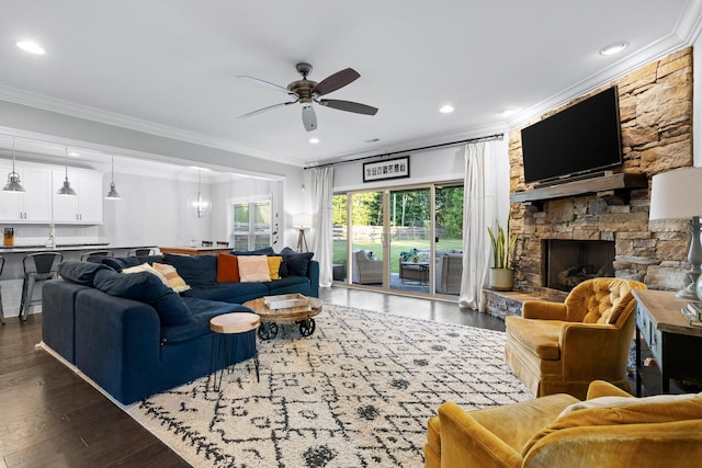 living room featuring dark hardwood / wood-style flooring, ceiling fan, a stone fireplace, and crown molding