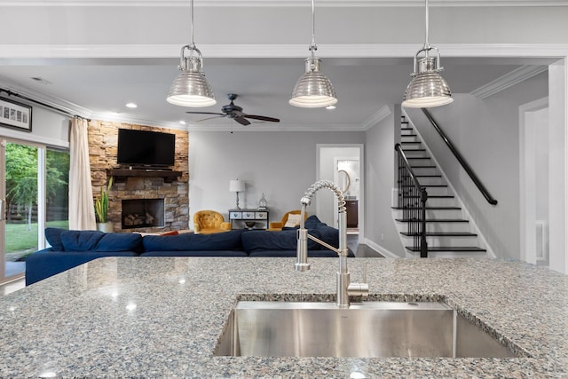 kitchen featuring pendant lighting, sink, ornamental molding, a fireplace, and light stone counters